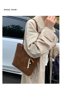 Brown leather tote bag worn by model in trench coat with wooden bead charm detail