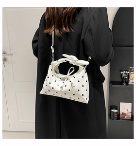 Detailed back view of white polka dot bag with bow handle on black trench coat outfit