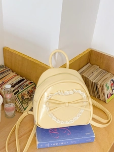 Petit sac à dos jaune avec dentelle cœur et nœud en cuir sur des livres anciens