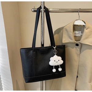 Close-up of black leather tote bag featuring a white plush cloud charm and spacious interior