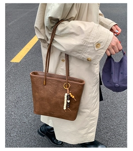 Detail of vintage brown leather tote bag with wooden bead charm on city background