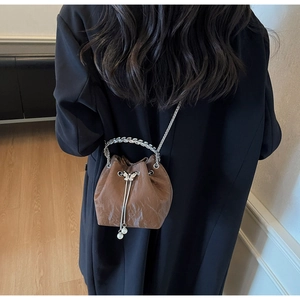 Détail d'un sac seau marron avec papillon métallique et pompon en perles