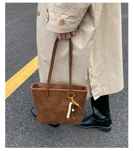 Close-up of vintage brown leather tote bag with stylish bead charm and zipper detail