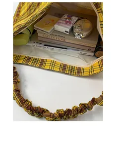 Detail of yellow plaid tote bag showing spacious interior with books and ruffled strap