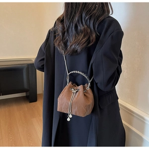 Sac seau marron texturé avec chaîne argentée et breloque perle porté à l'épaule