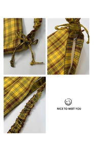 Detail of yellow plaid tote bag with drawstring closure and ruched shoulder strap texture