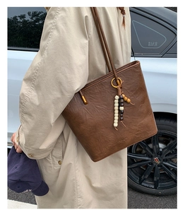 Close-up of brown vintage leather tote bag with stylish beaded pendant and slim shoulder straps