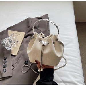 Détail du sac seau crème montrant la poignée florale argentée et le fermoir perle