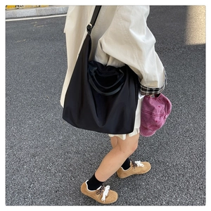 Street style shot of a large black nylon tote bag with adjustable shoulder strap detail