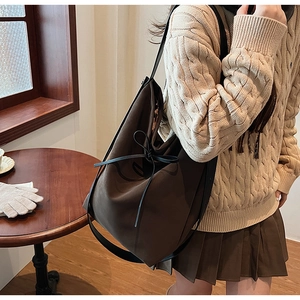 Detail of a large dark brown suede tote bag with a black bow in a cozy cafe setting