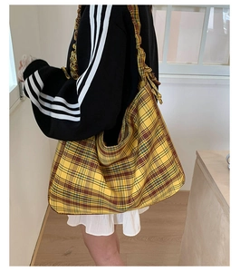Detail of yellow plaid tote bag featuring artistic pleated shoulder strap on model