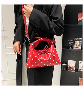 Close-up of red and white polka dot dumpling bag with bow handle and shoulder strap