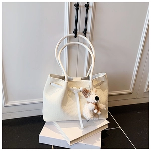 Détail du cabas blanc tissé avec une breloque d'ours en peluche et un bonnet marron