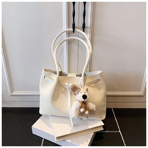 Détail macro du sac cabas tissé blanc crème avec une breloque en peluche pour chiot