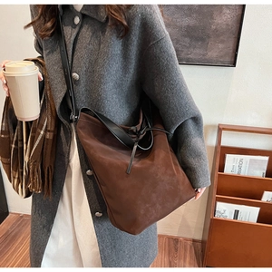 Brown suede bucket bag with adjustable black leather strap shown in a lifestyle setting