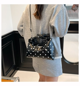 Close-up of black leather polka dot handbag with knot bow handle and adjustable strap