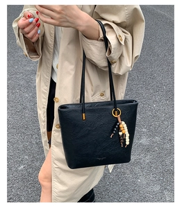 Detail of black leather tote bag featuring a beaded charm and fashion text on beige trench coat