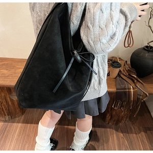 Detail of black suede tote bag with side bow decoration shown on a model