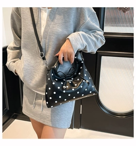 Detail of black polka dot crossbody bag with drawstring closure and silver metal pendant