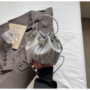 Détail du sac seau argenté avec texture métallisée froissée et boucle papillon en métal