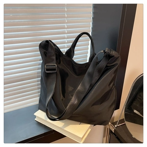 Detail of minimalist black nylon tote bag with wide adjustable shoulder strap on books