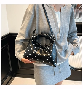 Detailed side view of a black polka dot crossbody bag with a unique knot handle and bow