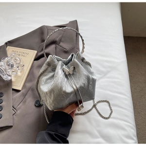 Détail du sac seau argenté avec ornement papillon, cordon perlé et bandoulière chaîne