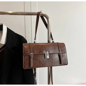 Detailed view of brown rectangular faux leather bag with silver metal buckle on a rack