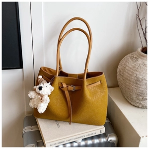 Détail du cabas tressé jaune moutarde avec breloque ours en peluche sur une valise