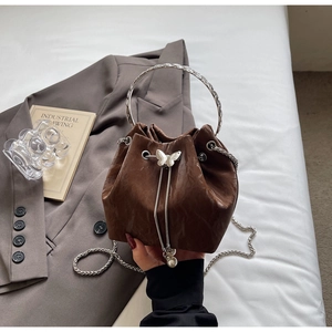 Détail d'un sac seau marron avec ornement papillon argenté et accents de perles