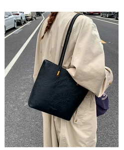 Detail of black wrinkled leather tote bag with gold hardware shown on a city street