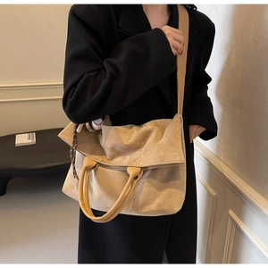 Detail of a beige oversized tote bag with brown leather handles and a baseball charm