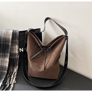 Close-up of brown suede bucket bag featuring black leather bow and wide shoulder strap