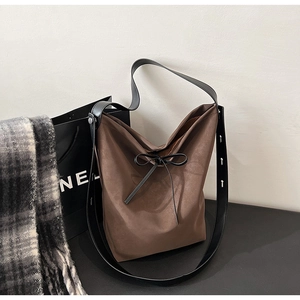Detail of coffee brown bucket bag showing matte leather texture and delicate bow tie