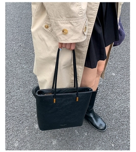 Detail view of black faux leather tote bag with long straps on minimalist trench coat outfit