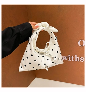 Detailed view of white polka dot handbag featuring knotted handle and drawstring detail
