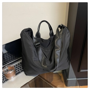 Large black nylon tote bag with wide strap on a desk with a laptop for daily commuting