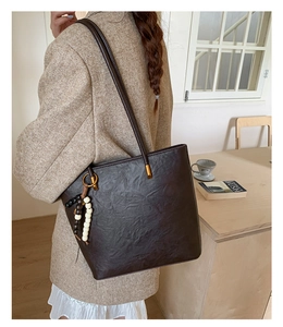Detail of a dark brown tote bag with leather texture and bead tassel accessory