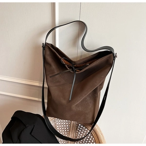 Close-up of a brown tote bag with a small bow detail placed on a woven chair