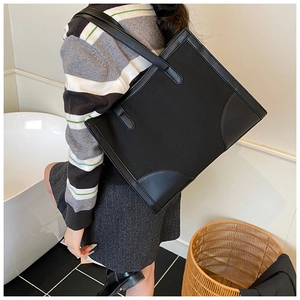 Détail d'un grand sac fourre-tout noir en toile avec bordure en cuir porté sous le bras