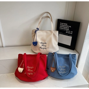 Detailed view of canvas tote bags in cream, red, and blue with letter print and mini pouches