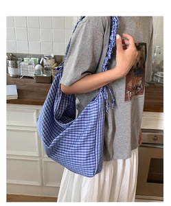 Detail of blue and white plaid hobo bag featuring pleated shoulder strap and side ties