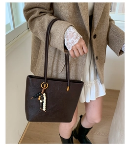 Detail of dark brown leather tote bag with vintage texture and wooden bead tassel