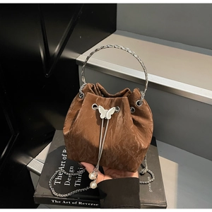 Détail du sac seau marron texturé avec pendentif perle et breloque papillon sur livre