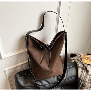 Detail of dark brown suede bucket bag featuring black leather tie and adjustable strap