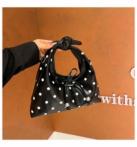 Detail of black polka dot handbag featuring a knotted handle and silver metal charms