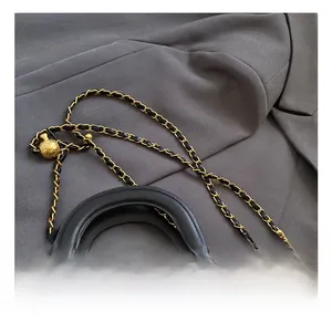 Detail of brown quilted bag with gold adjustable ball and chain strap on grey fabric