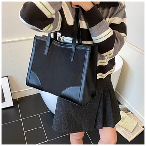 Détail d'un grand sac fourre-tout en toile noire avec patchwork en cuir et coins renforcés