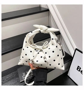 Close-up of white leather handbag with black polka dots and metal ball drawstring bow