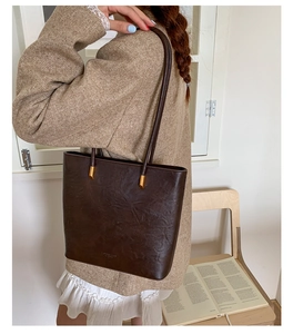 Detail of dark brown tote bag with pleated leather texture and gold metal hardware